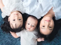 A baby lying between two older siblings on a rug