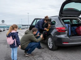 Family inspecting a hire car and fitting a child seat before leaving an airport collection bay