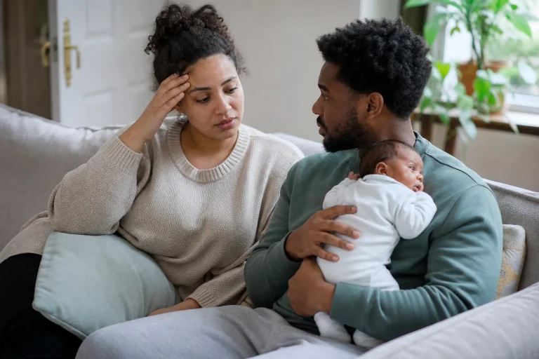Tired new parent talking with a supportive partner holding their awake baby